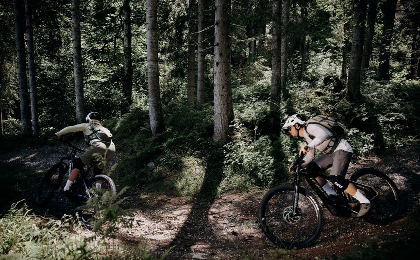 Twee mountainbikers fietsen op een bospad door schaduwrijke bossen