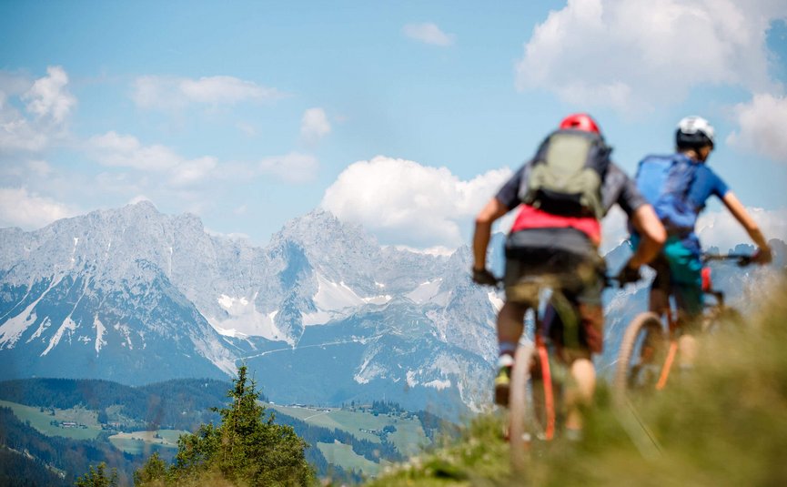 Zwei Radfahrer fahren auf einem bergigen Pfad mit Alpen im Hintergrund