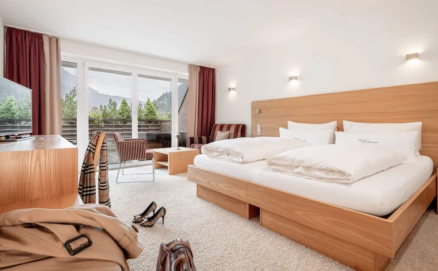 Helles Hotelzimmer mit großem Bett und Balkon mit Bergblick