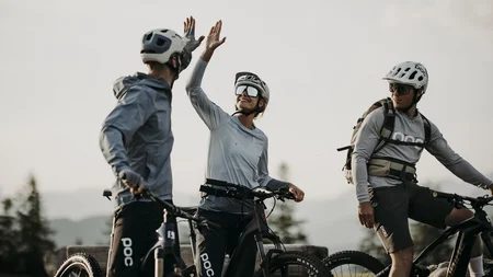Drei Fahrradfahrer in Helmen geben sich Highfive im Freien