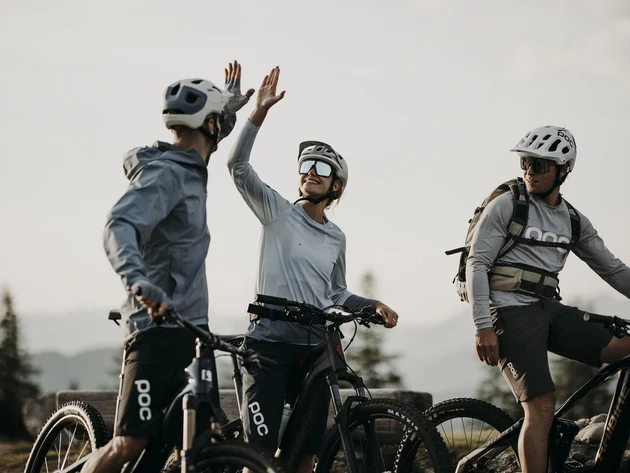 Was steckt hinter dem Umweltengagement von Bikehotels? Drei Fahrradfahrer in Helmen geben sich Highfive im Freien