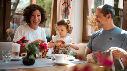 Familie mit Kind genießt Kaffee und Kuchen am Küchentisch