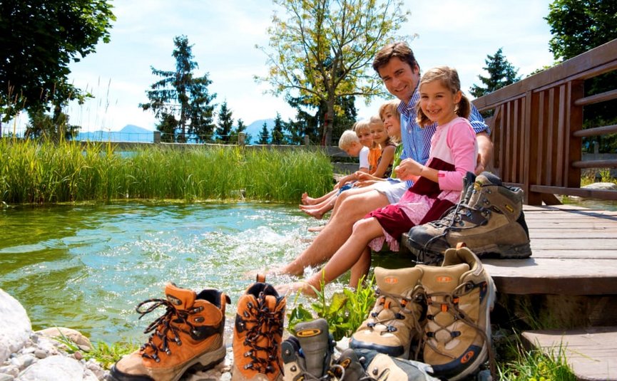 FAMILY PACKAGE Family sitting by lake with feet in water and hiking boots on shore