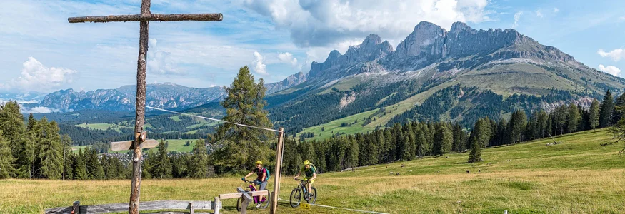 Dolomiten - Eggental © WOM Medien - Andreas Meyer Fahrradfahrer in den Bergen mit großem Holzkreuz und Blick auf Alpengipfel