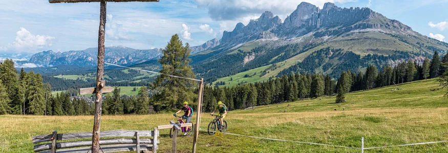 Fahrradfahrer in den Bergen mit großem Holzkreuz und Blick auf Alpengipfel