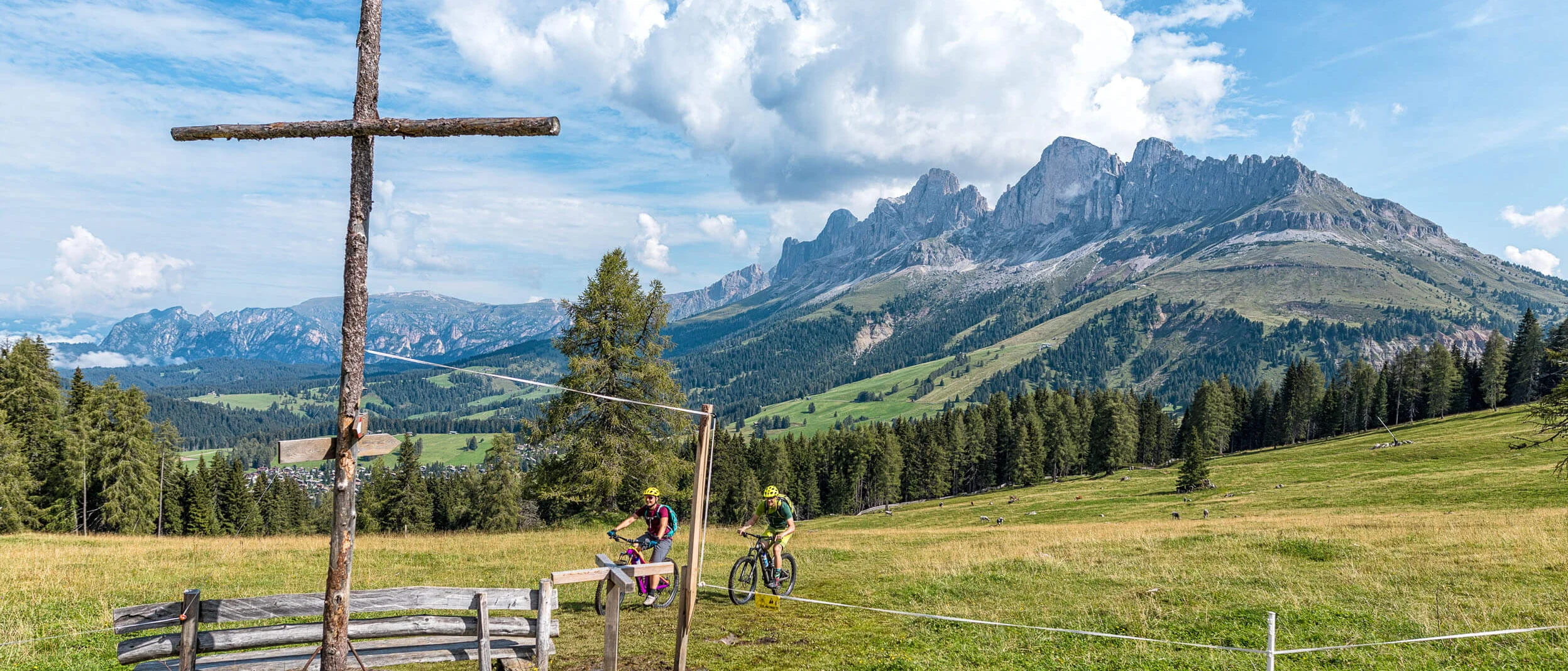 Cyclists in the mountains with wooden cross and Alpine peaks in background