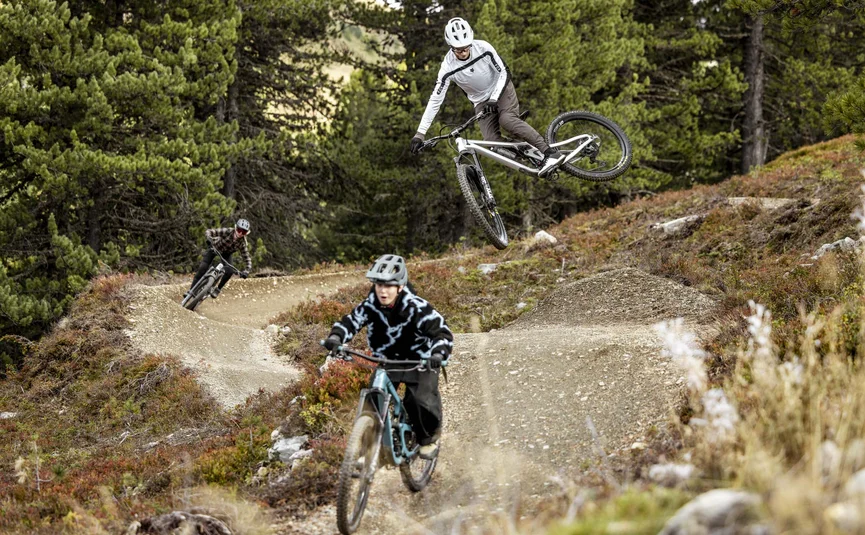 Drei Mountainbiker fahren auf einem schlammigen Bergpfad in einem bewaldeten Gebiet