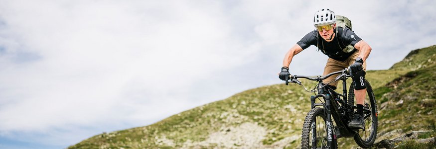 Mountainbiker fährt auf felsigem Bergpfad bei bewölktem Himmel