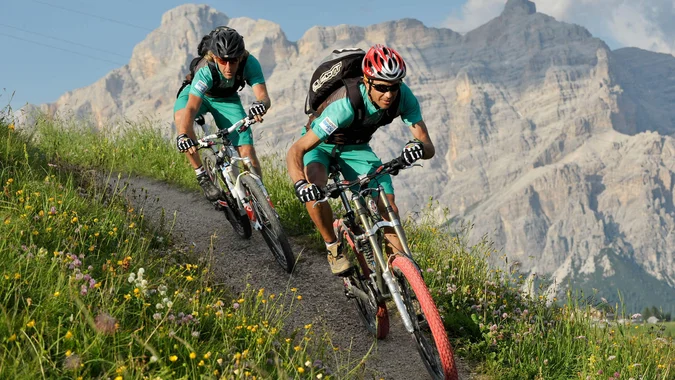 Zwei Mountainbiker fahren auf einem Bergpfad vor Felsen