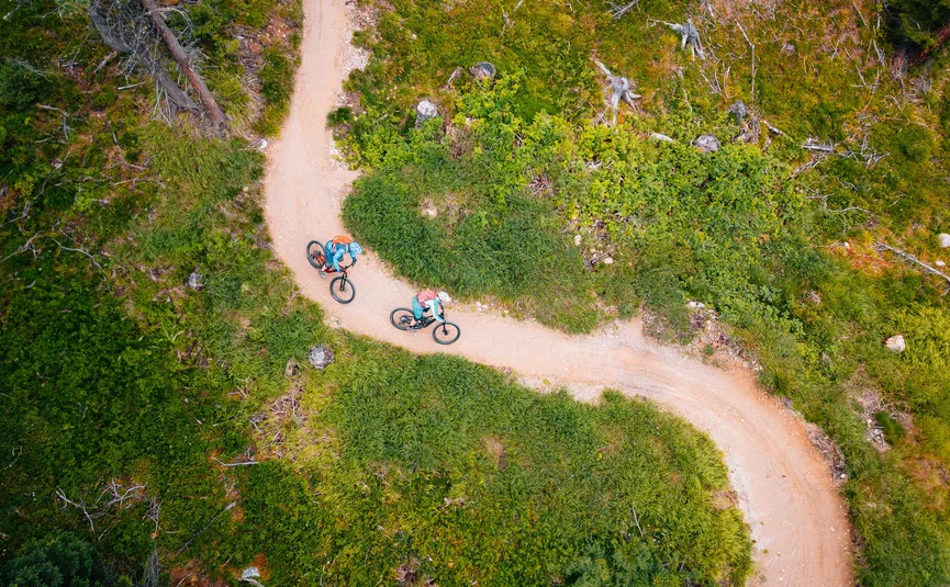Two cyclists on a narrow forest trail viewed from above