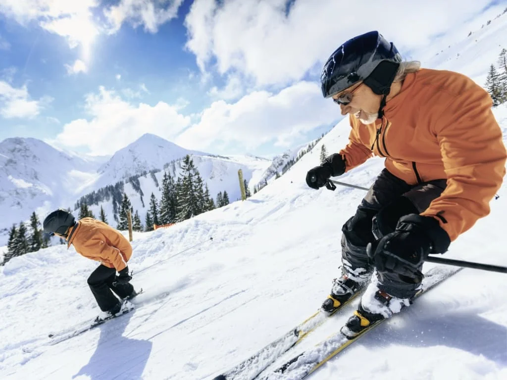 Zwei Skifahrer in orange Jacken fahren einen verschneiten Berg hinunter