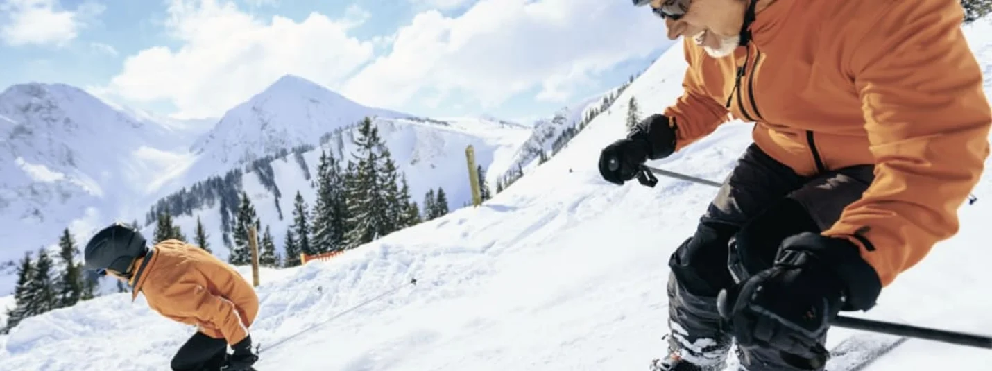 Two skiers in orange jackets skiing down a snowy mountain