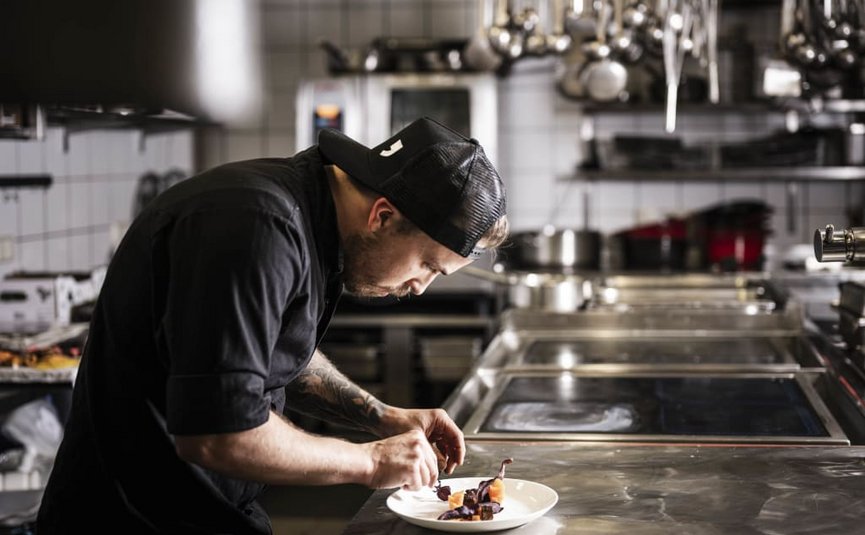 Chef plating food on a plate in a commercial kitchen