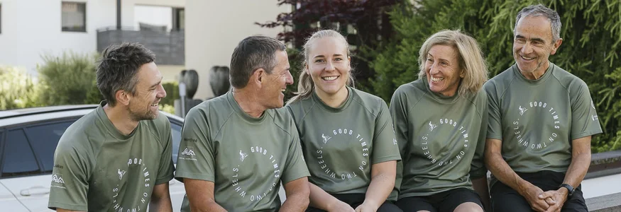 Hotel Innerhofer *** © Armin Terzer Fünf Personen in grünen T-Shirts sitzen lachend auf einer Mauer vor einem Hotel