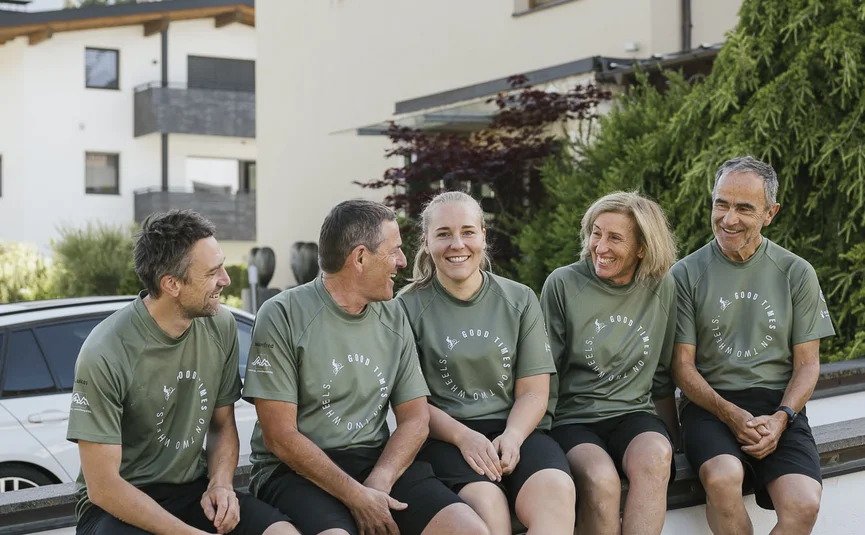 Hotel Innerhofer *** © Armin Terzer Fünf Personen in grünen T-Shirts sitzen lachend auf einer Mauer vor einem Hotel