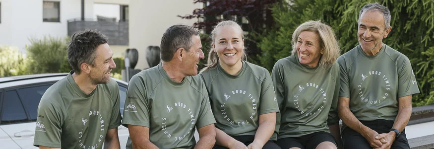 Hotel Innerhofer *** © Armin Terzer Vijf mensen in groene shirts zittend en lachend op een muur voor een hotel