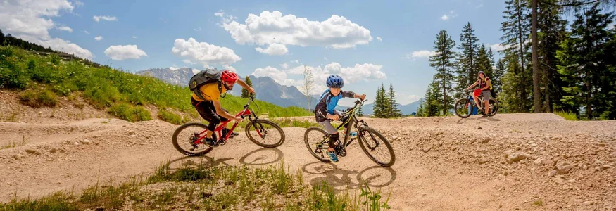 Drie personen mountainbiken op een heuvelachtig pad onder een zonnige lucht