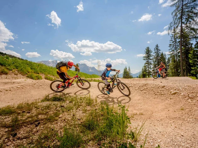 Three people mountain biking on a hilly trail under a sunny sky