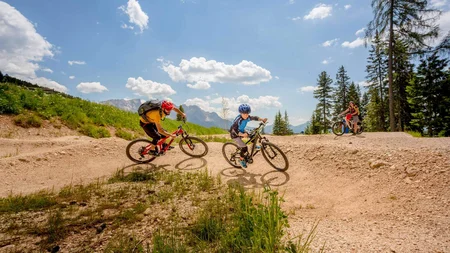 Three people mountain biking on a hilly trail under a sunny sky