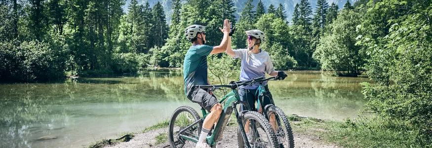 Twee fietsers geven elkaar een high five bij een bergmeer