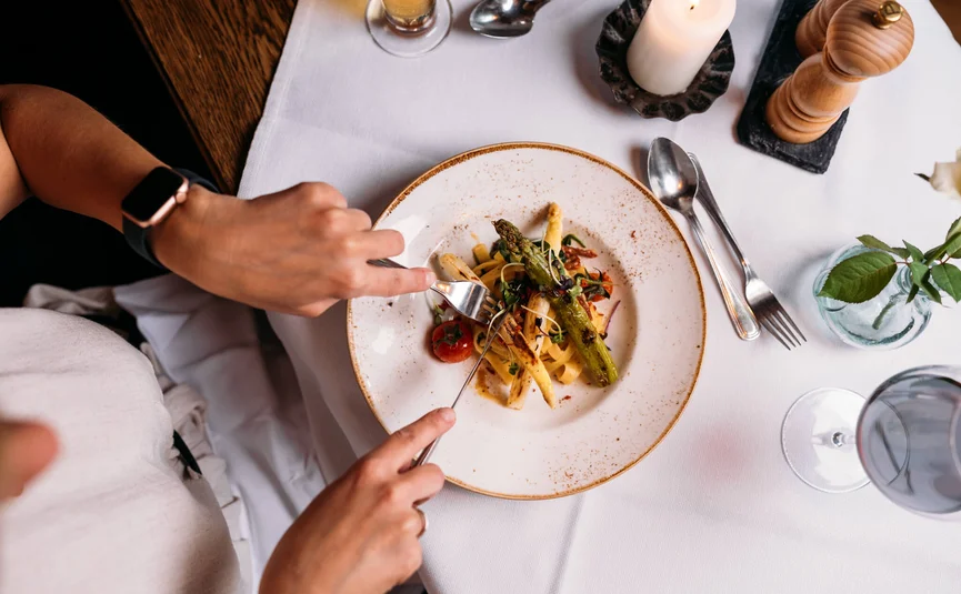 Person isst Spargel mit Gabel und Messer in gehobenem Restaurant