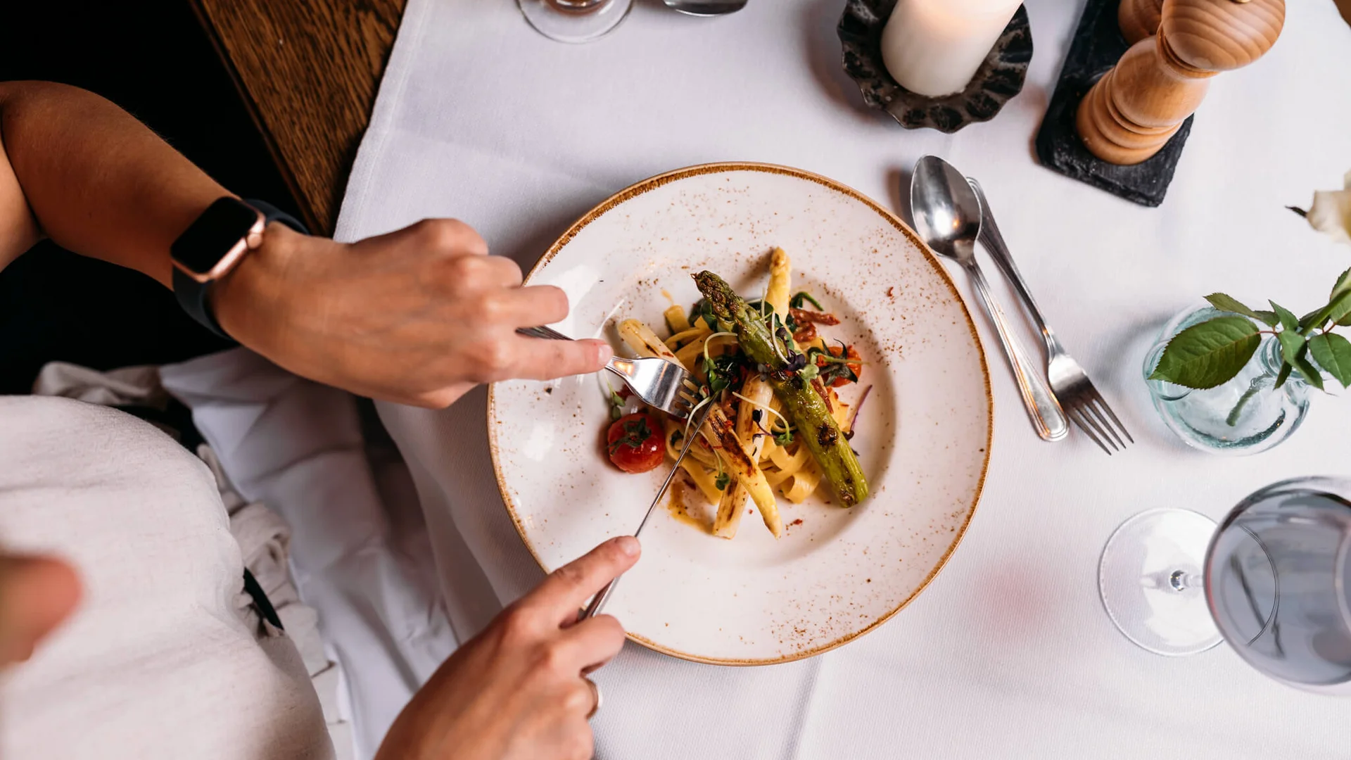 Person isst Spargel mit Gabel und Messer in gehobenem Restaurant