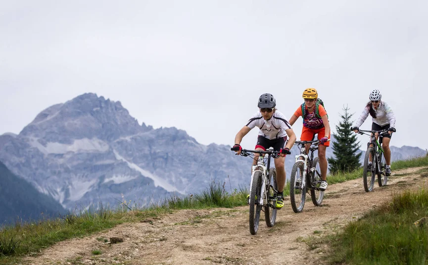 Drei Mountainbiker fahren auf einem Bergweg mit Bergen im Hintergrund