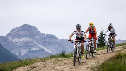 Drei Mountainbiker fahren auf einem Bergweg mit Bergen im Hintergrund