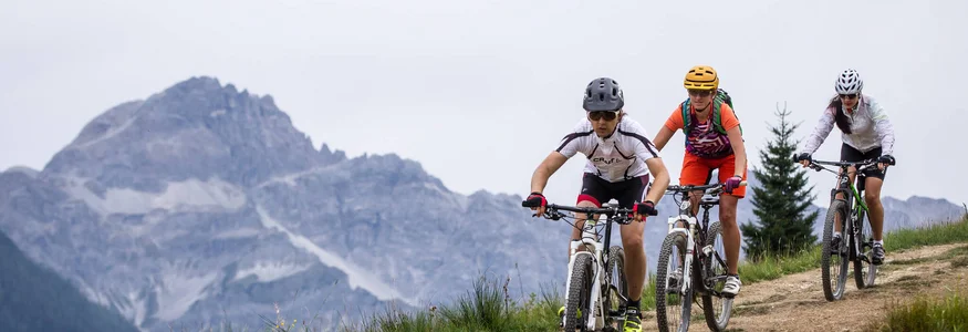 Drei Mountainbiker fahren auf einem Bergweg mit Bergen im Hintergrund