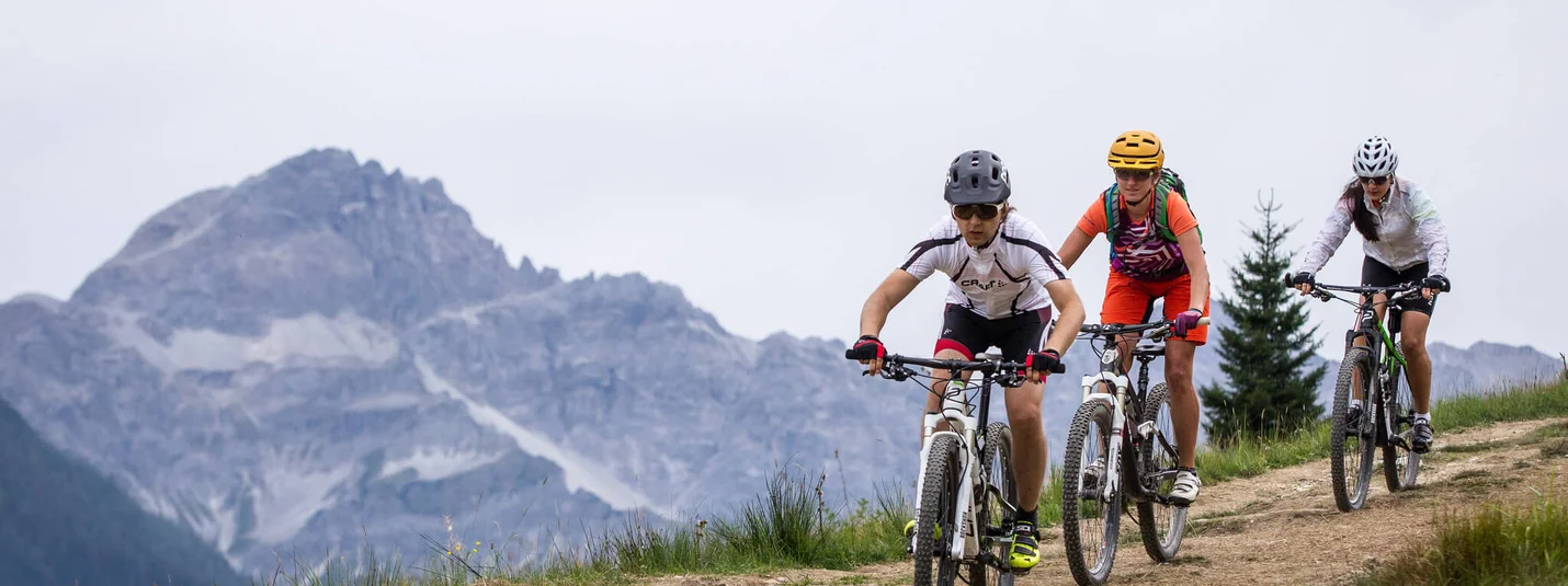 Three mountain bikers riding on a trail with mountains in the background