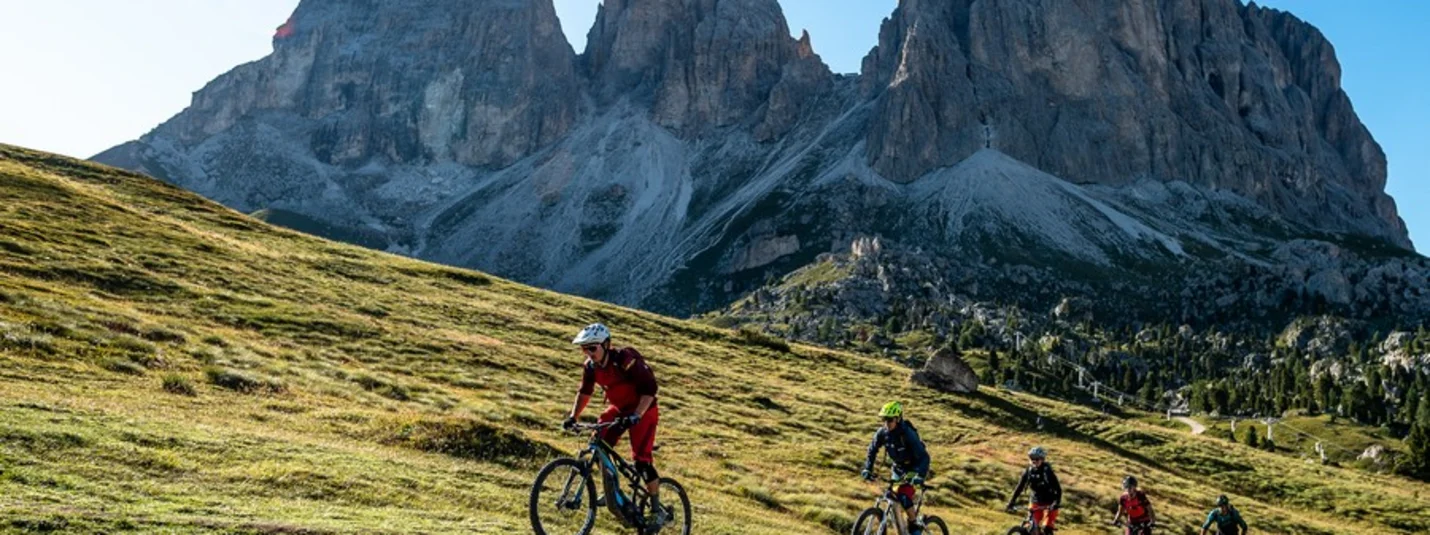 Five mountain bikers riding on a trail with rocky mountains in the background