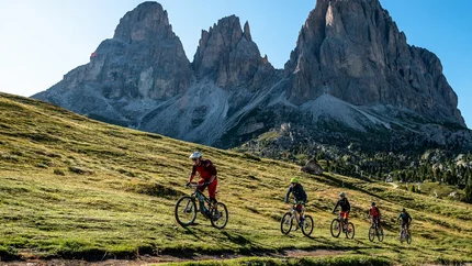 Fünf Mountainbiker fahren auf einem Bergpfad mit Felsbergen im Hintergrund