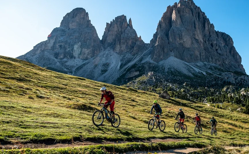 Fünf Mountainbiker fahren auf einem Bergpfad mit Felsbergen im Hintergrund