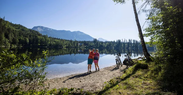 Meerdaagse tours © Velontour Twee fietsers maken een selfie aan het meer met bergen op de achtergrond