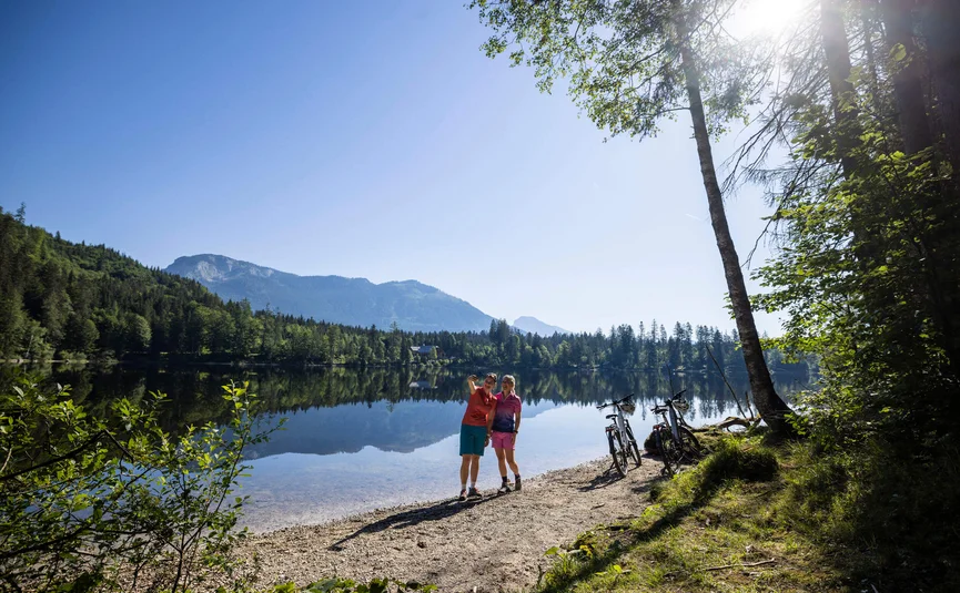 Two cyclists taking a selfie by the lake with mountains in the background