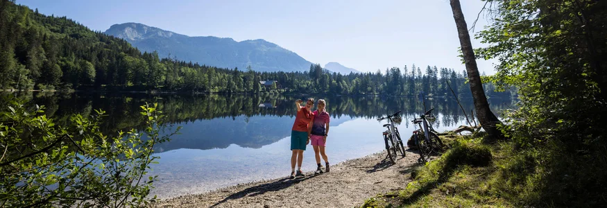 Twee fietsers maken een selfie aan het meer met bergen op de achtergrond