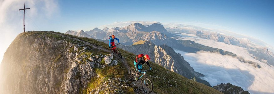 Zwei Mountainbiker auf Bergpfad nahe Gipfelkreuz in den Alpen