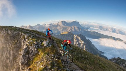 Zwei Mountainbiker auf Bergpfad nahe Gipfelkreuz in den Alpen