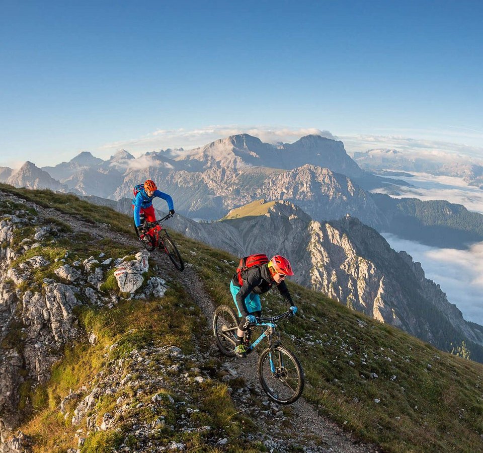 Mountainbike-Saisonstart am Kronplatz © WOM Medien - Andreas Meyer Zwei Mountainbiker auf Bergpfad nahe Gipfelkreuz in den Alpen
