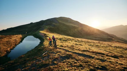 Zwei Mountainbiker fahren auf einem Bergweg bei Sonnenuntergang
