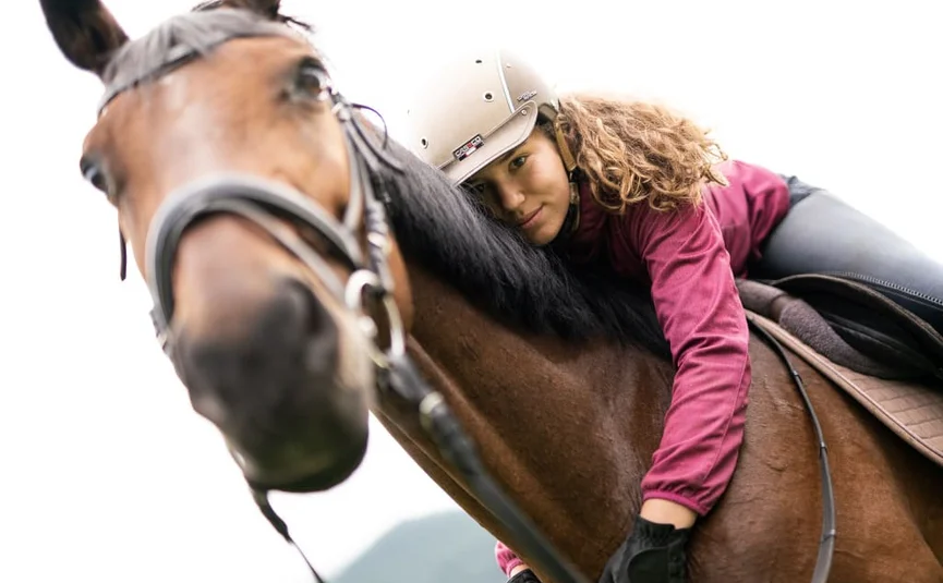 Riding holiday at the GUTshof / 3 nights Rider wearing helmet lying on a brown horse outdoors