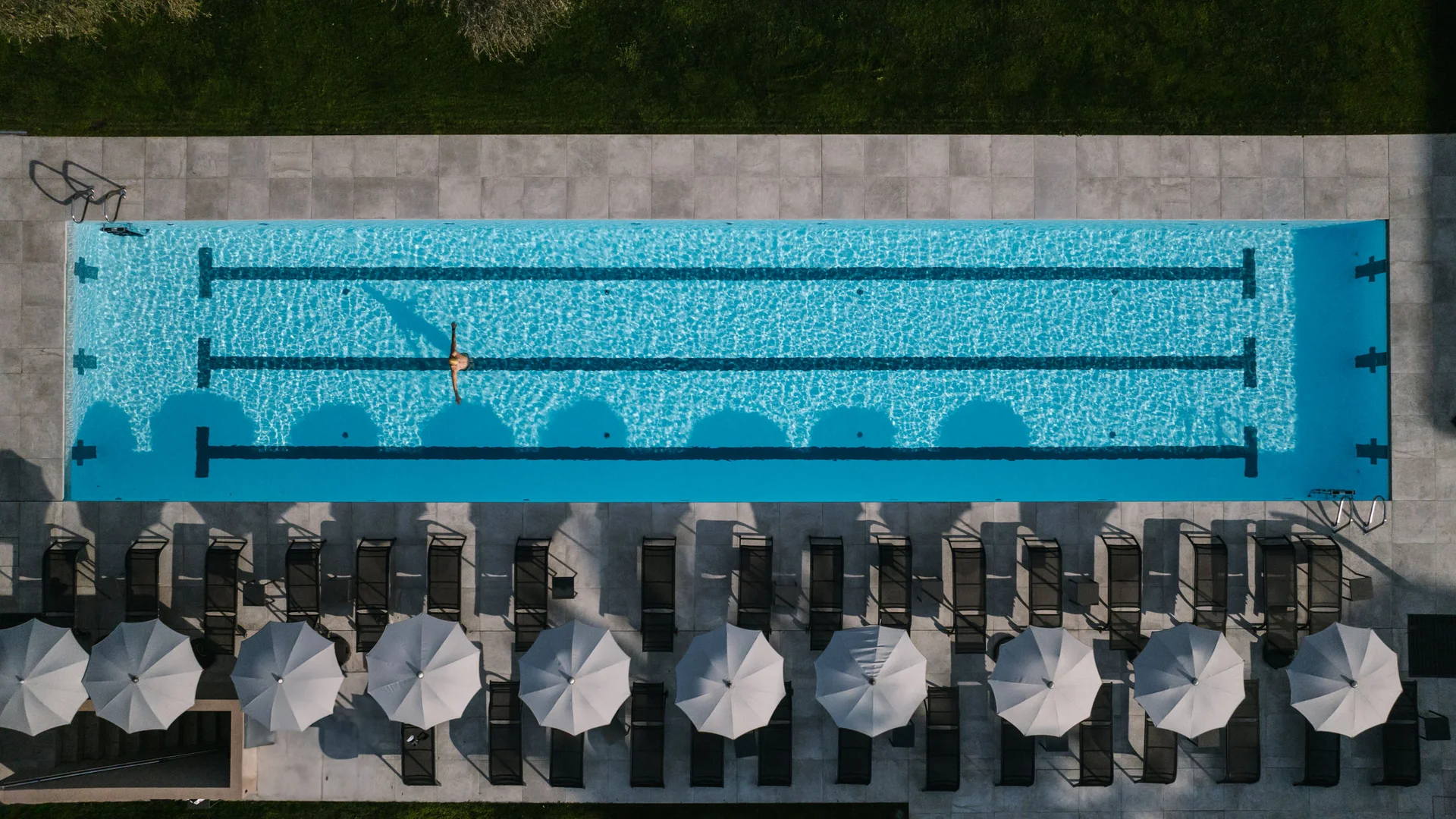 Luftaufnahme eines leeren Pools mit einer Person schwimmend und Sonnenschirmen daneben