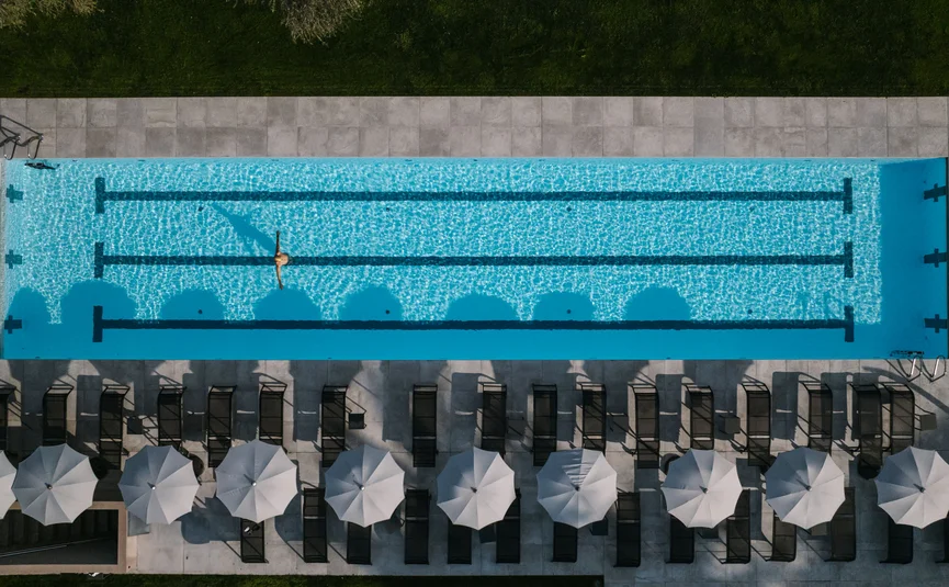 Aerial view of empty swimming pool with one swimmer and umbrellas alongside