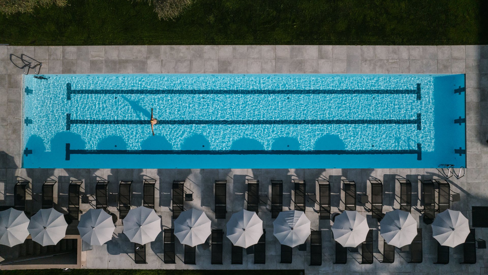 Luftaufnahme eines leeren Pools mit einer Person schwimmend und Sonnenschirmen daneben