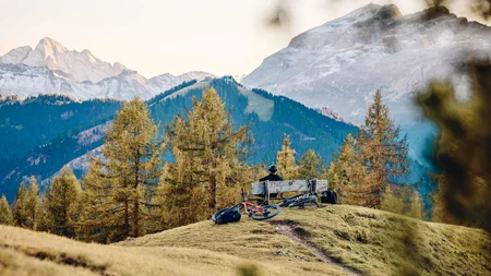 Mountainbike-Urlaub in Alta Badia © Tobias Köhler Person sitzt auf Bank in den Bergen mit zwei Mountainbikes und Wald im Hintergrund