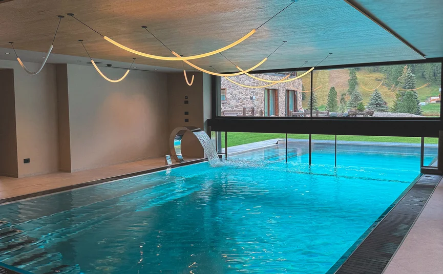 Modernes Hallenbad mit Wasserfall und Panoramablick auf Berge