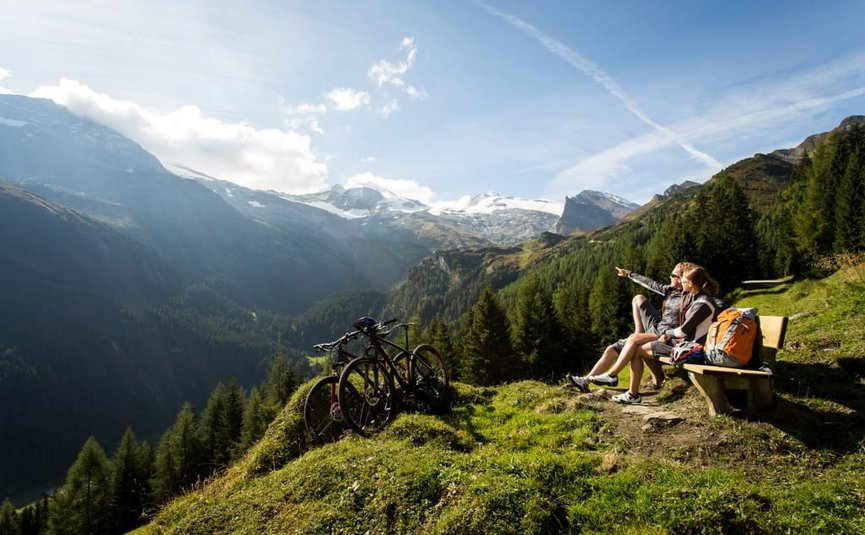 Two cyclists sitting on a bench enjoying mountain view