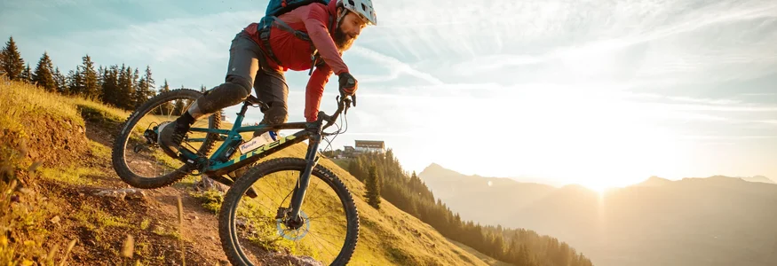 Mountainbiker fährt den Hang bei Sonnenuntergang hinab