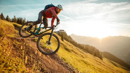 Mountainbiker fährt den Hang bei Sonnenuntergang hinab