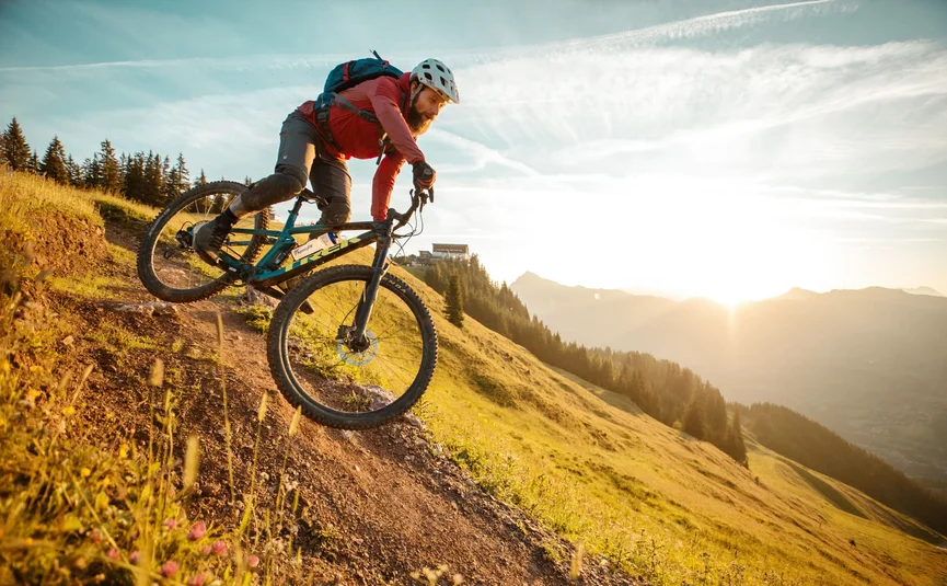 Hahnenkamm Trail © David Karg Mountainbiker fährt den Hang bei Sonnenuntergang hinab